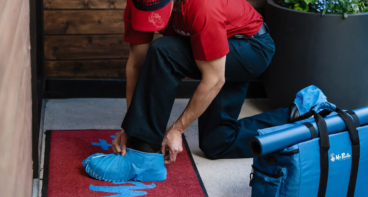 A Mr Rooter plumber putting on booties before entering a home.