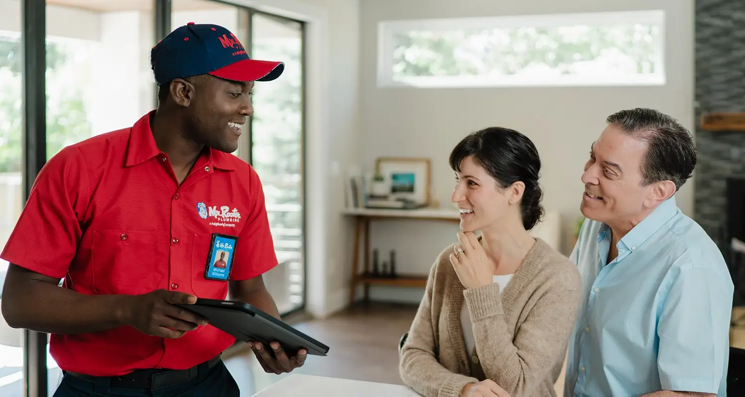 A plumber from Mr Rooter Plumbing talking and smiling with the home owners he helped.
