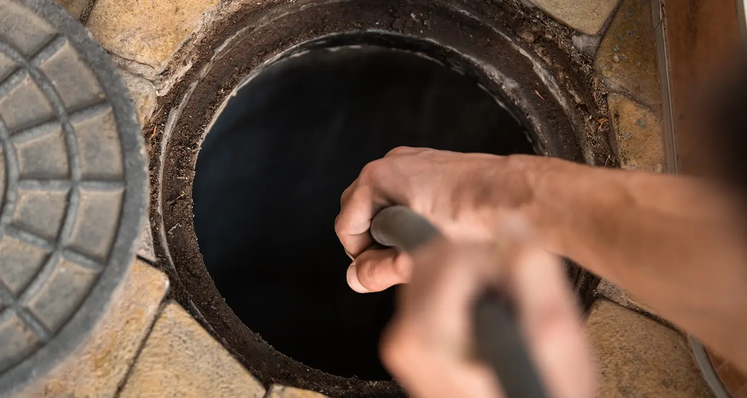 Hands holding a hose that is down an open sewage pipe.