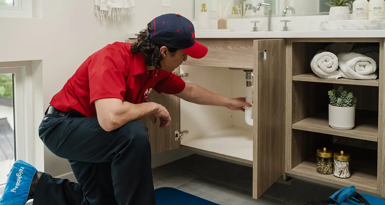 A plumber from Mr Rooter Plumbing inspecting under a bathroom sink.