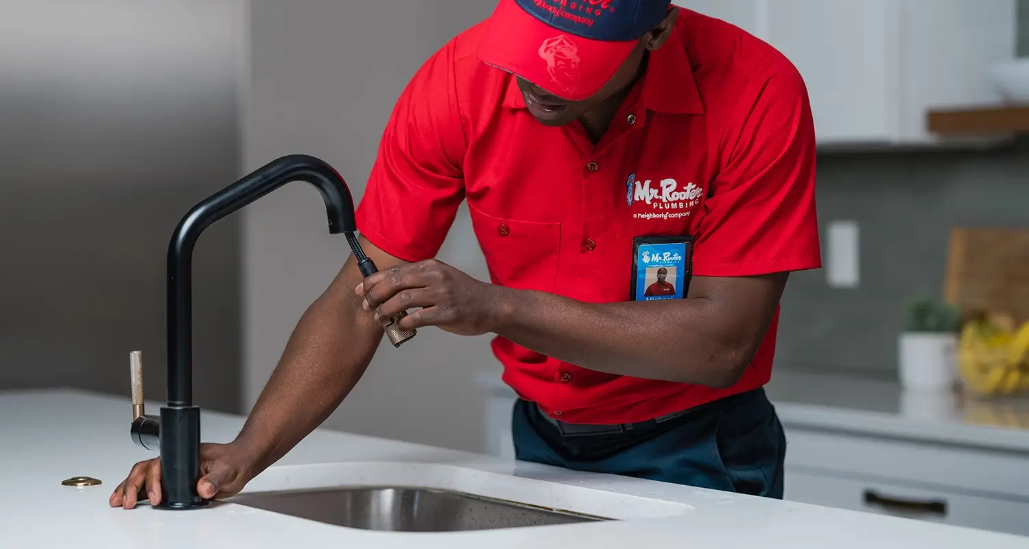 Mr Rooter Plumber working on the faucet of a modern kitchen sink.